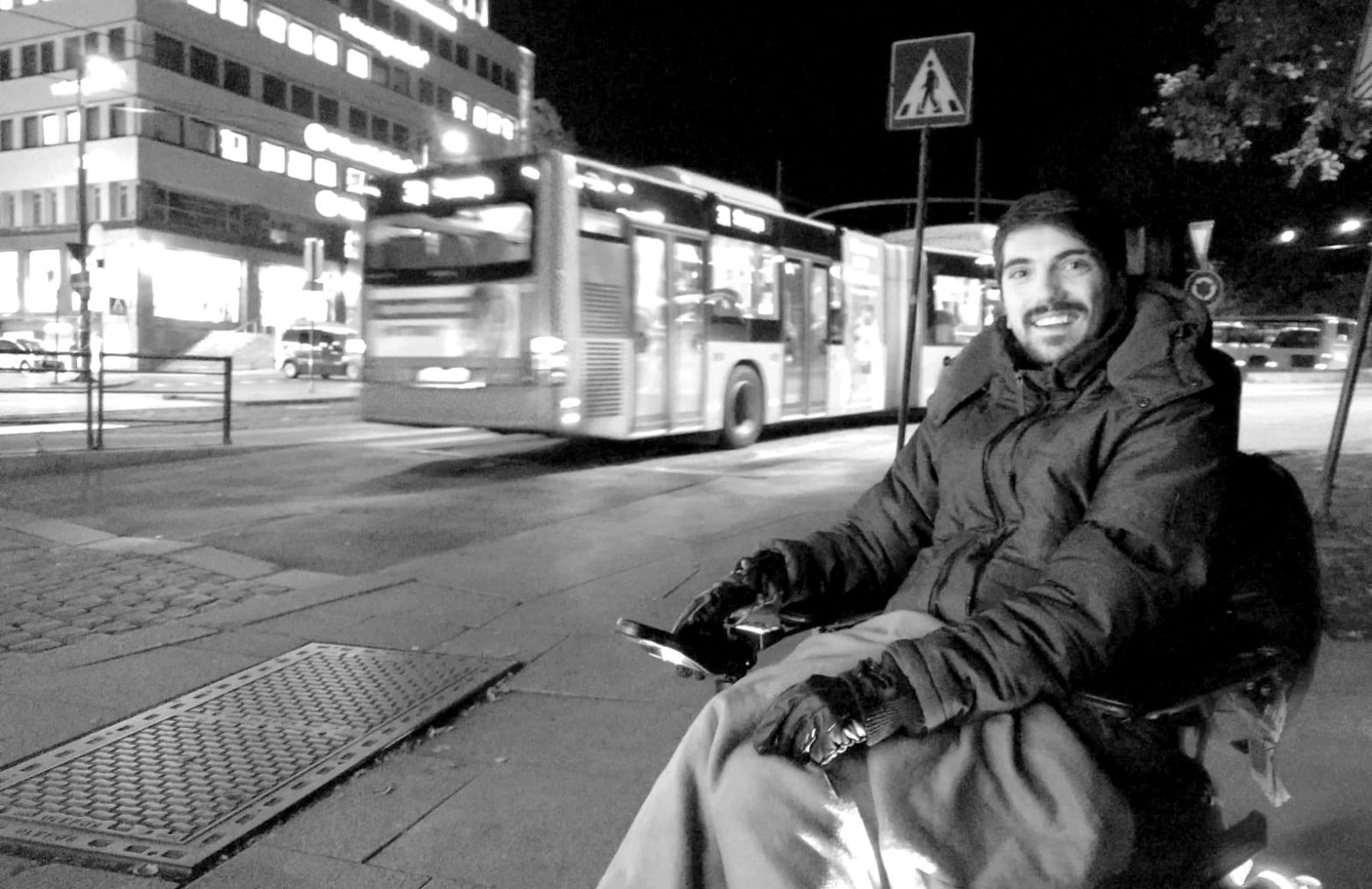 Amir i elektrisk rullestol på gata, med en buss i bakgrunnen.