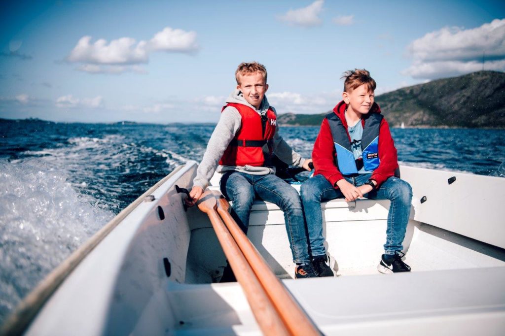 Henrik og Erik kjører båten. Henrik styrer. De har vind i håret og god fart.