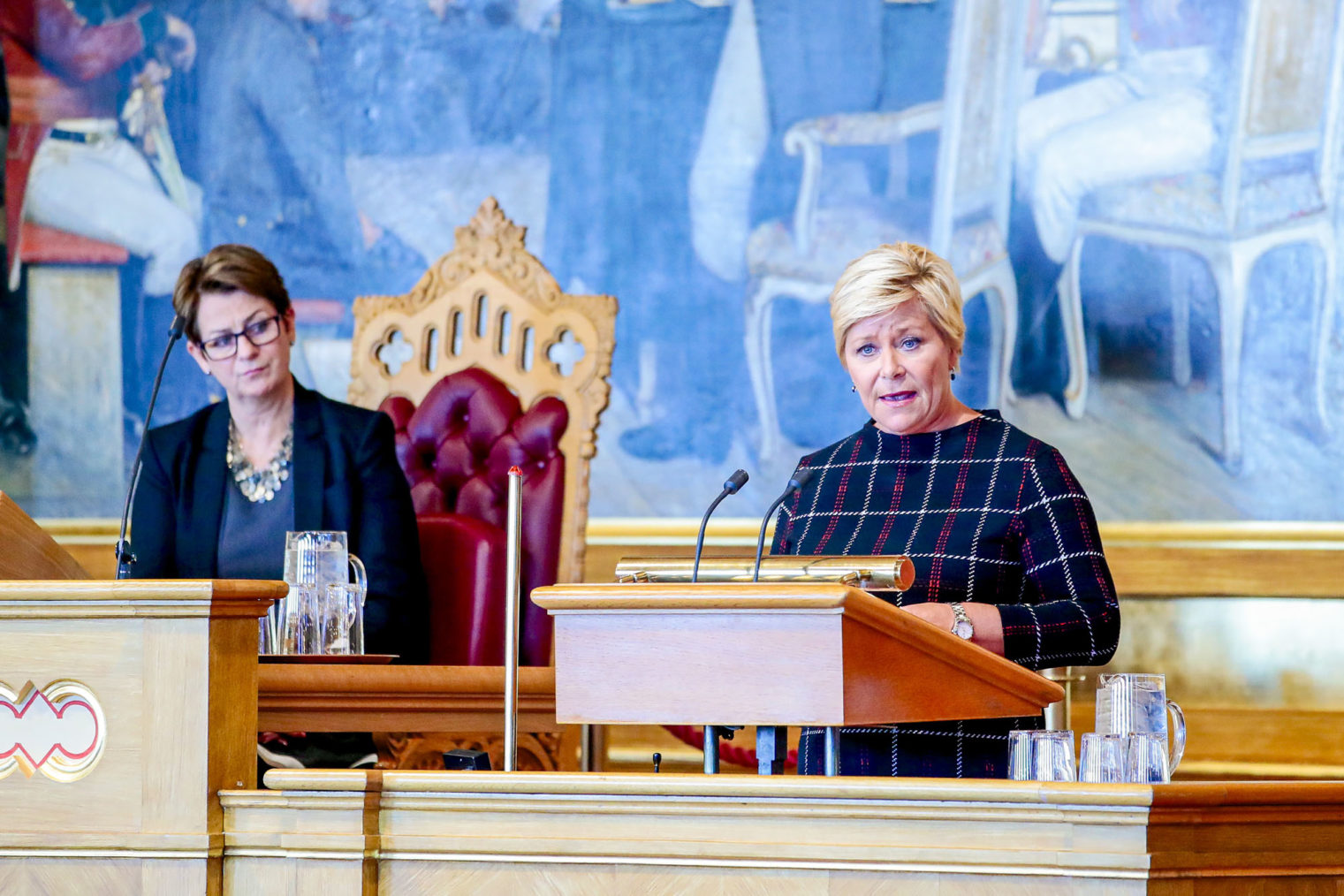 Siv Jensen på Stortingets talerstol. Stortingspresidenten følger med.