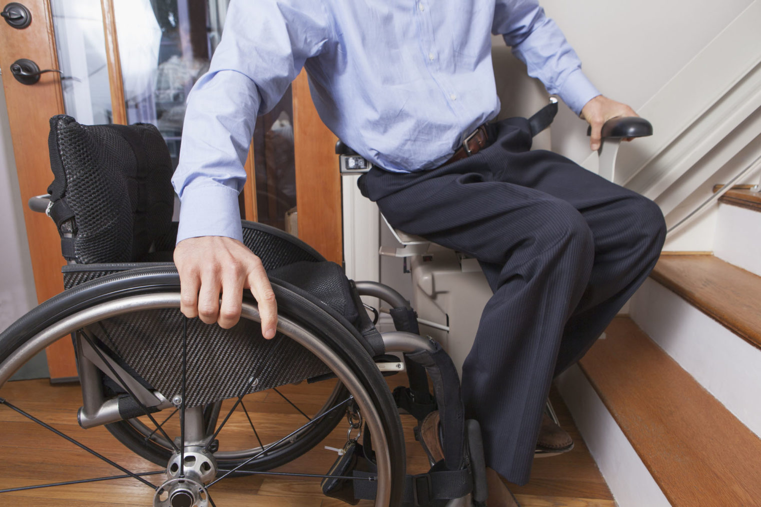 Detaljbilde av mann som beveger seg fra en rullestol over i en trappeheis.