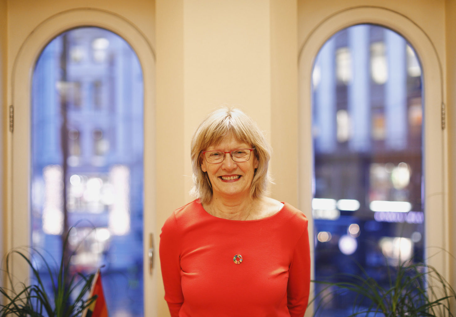 Karin Andersen fotografert på kontoret sitt på Stortinget, med utsikt til Karl Johans gate gjennom vinduene i bakgrunnen.