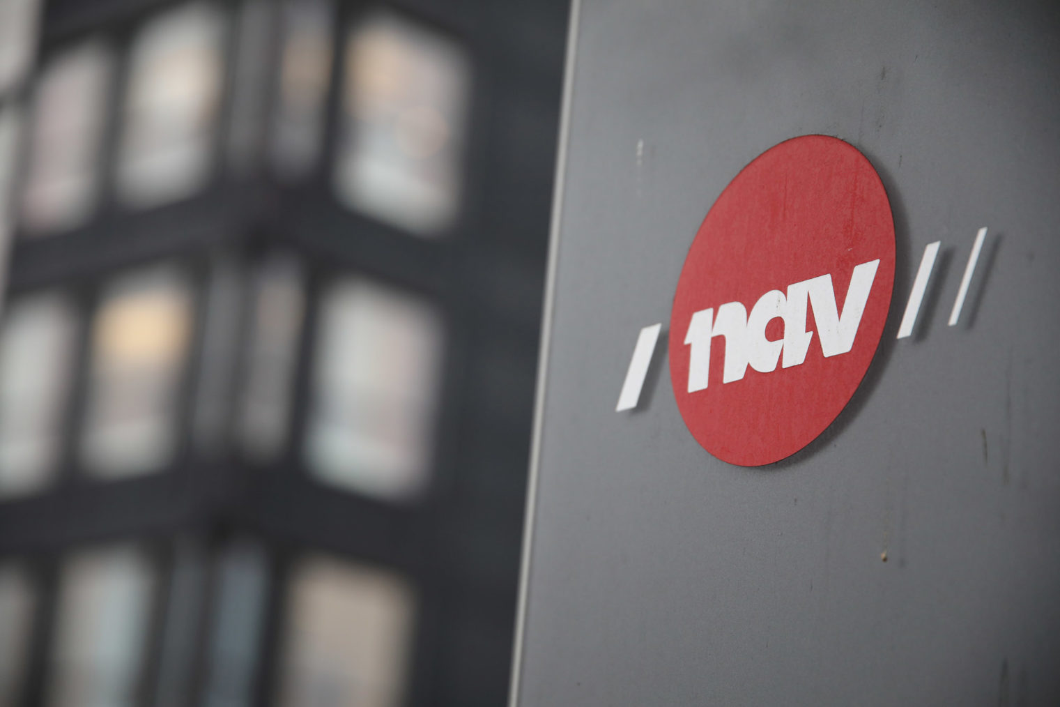Bilde av Nav-logo på vegg med kontorbygning i bakgrunnen.