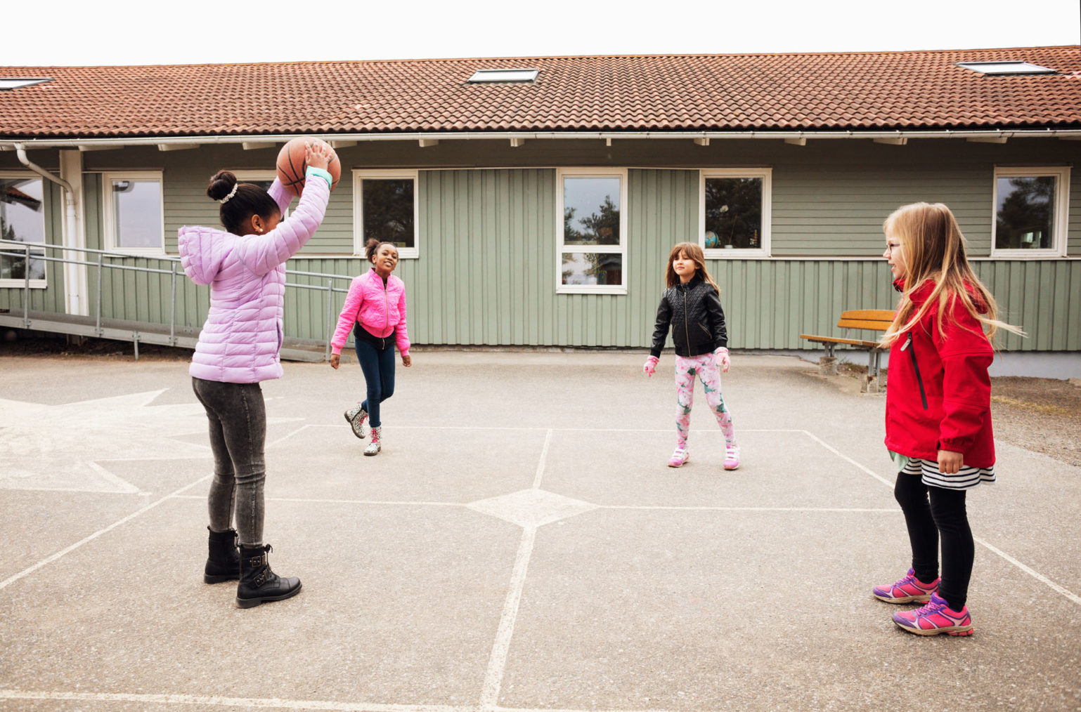 Bilde av barn som kaster ball i skolegård. Skolebygningen i bakgrunnen har rampe.