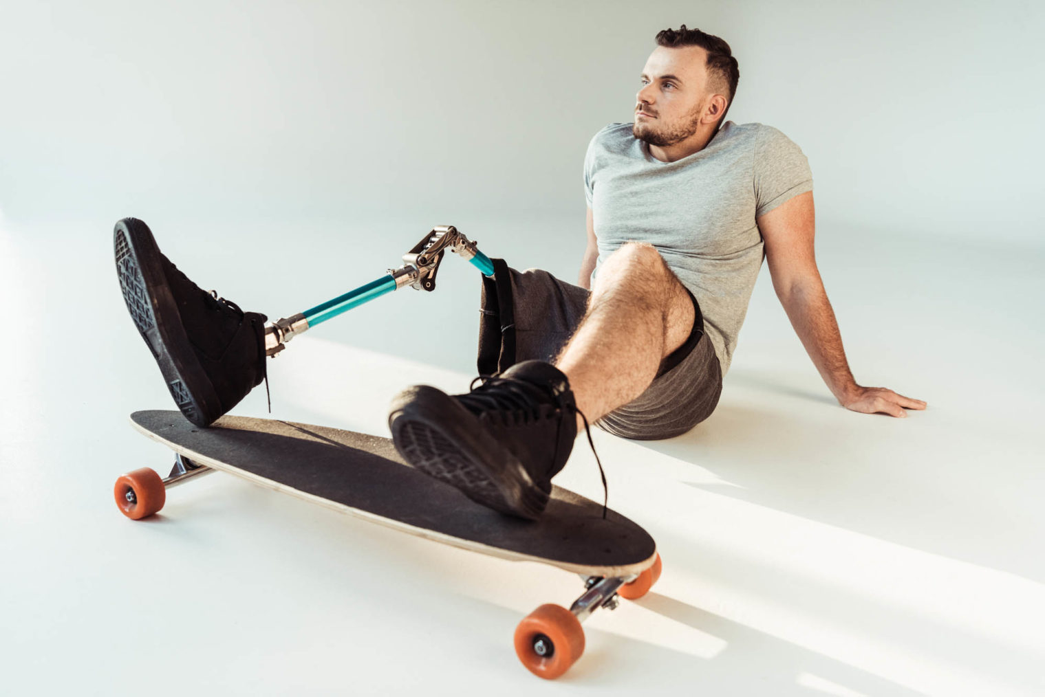 Ung mann med beinprotese og skateboard sitter avslappet på bakken.