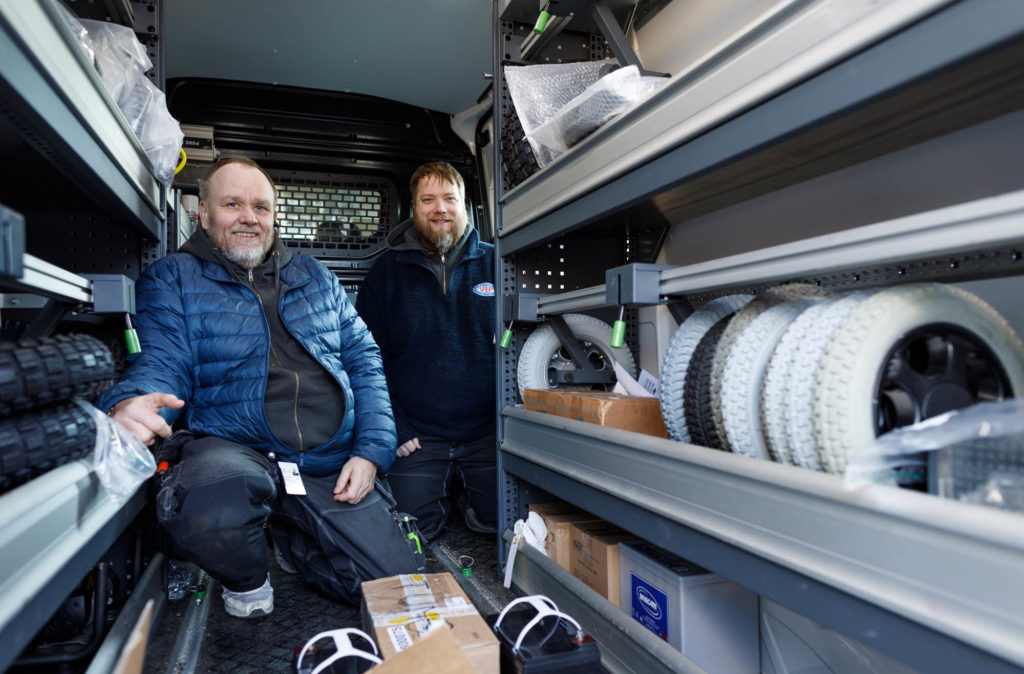 Pedersen og Lindgaard viser fram hyller med rullestolhjul inne i bilen.