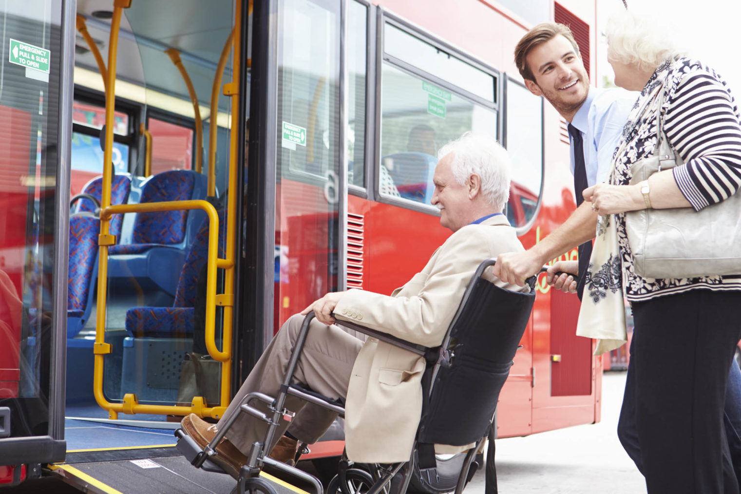 Bilde av bussjåfør som skyver eldre rullestolbruker opp rampe og inn på bussen.
