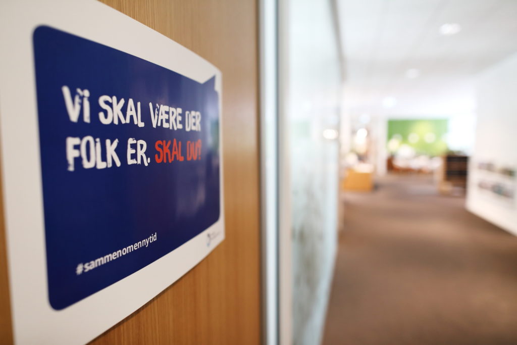 Bilde av kontordør med plakaten «Vi skal være der folk er. Skal du?». I bakgrunnen tomme kontorlokaler.