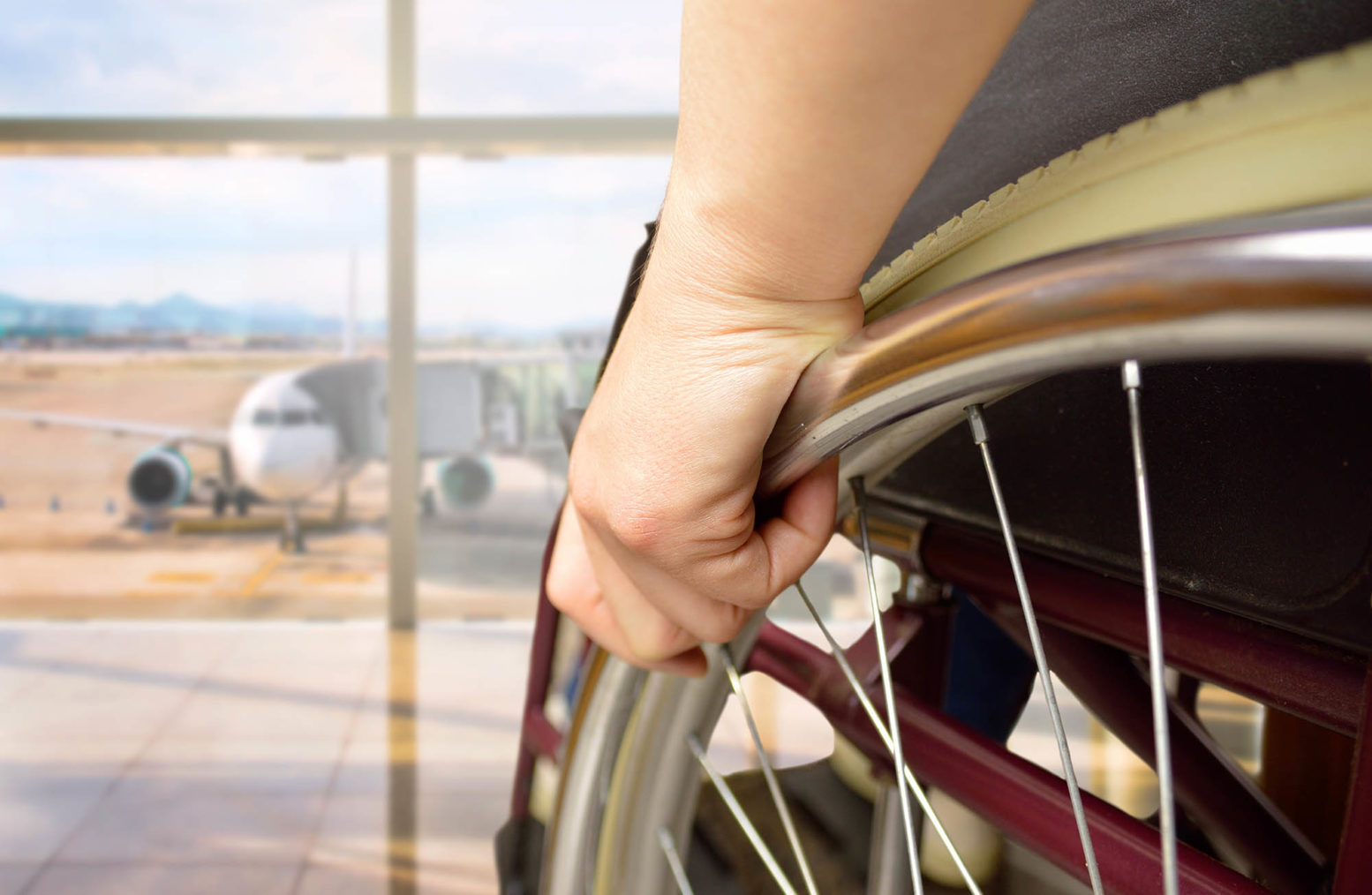 Detaljfoto av person i rullestol som ser ut fra terminalbygningen mot et parkert fly.