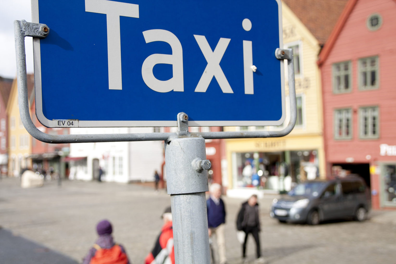 Nærbilde av taxi-skilt på holdeplass, med Bryggen i Bergen i bakgrunnen.