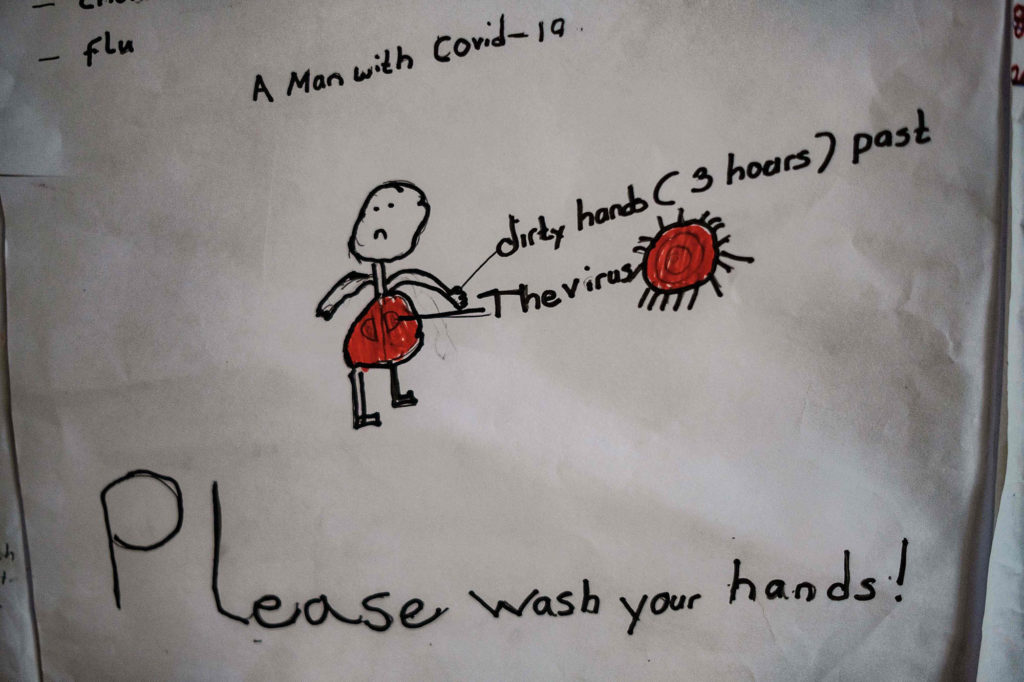 Barnetegning av en mann med virus på hendene. Teksten lyder: Please wash your hands.