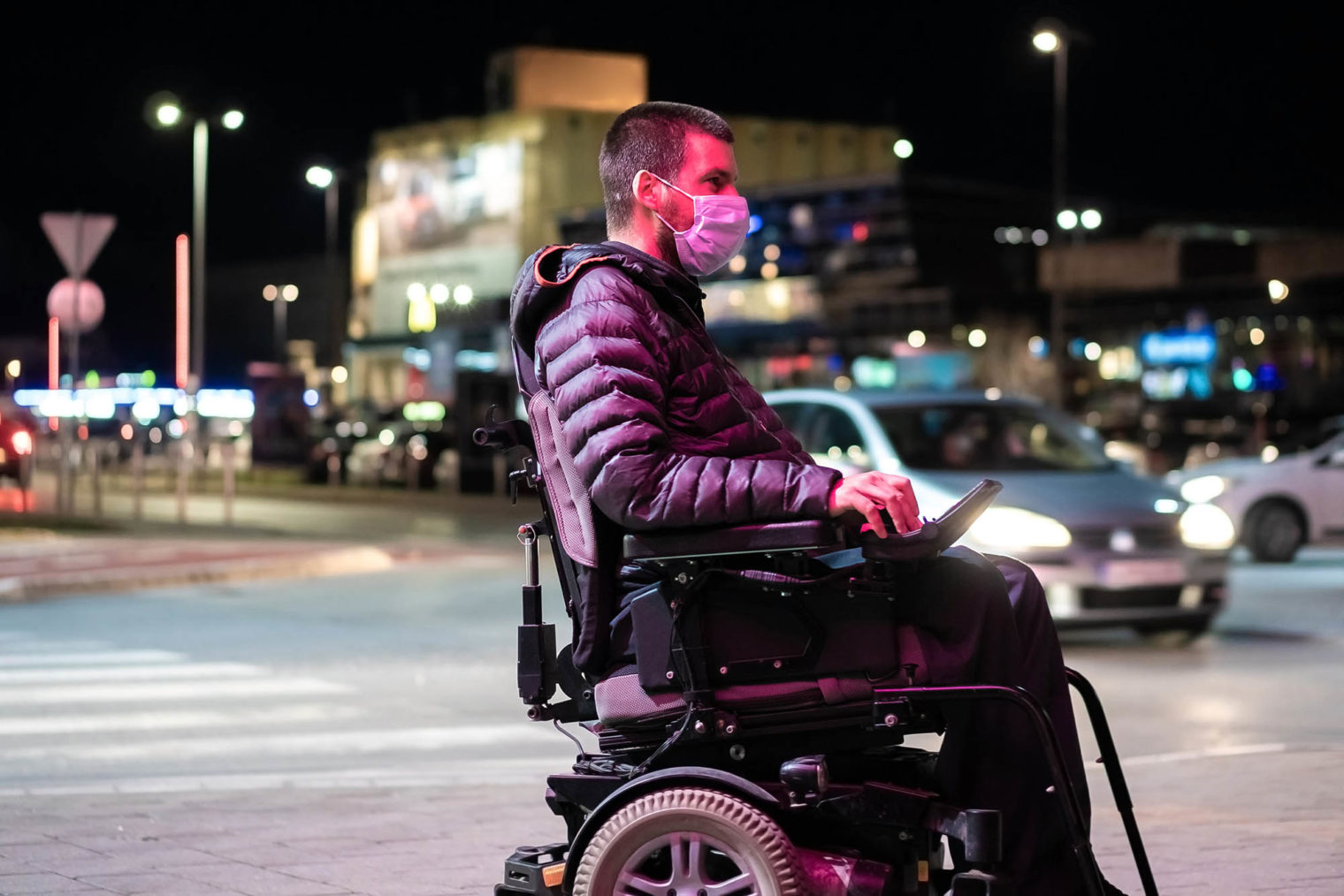 Ung mann med munnbind og elektrisk rullestol i bymiljø.
