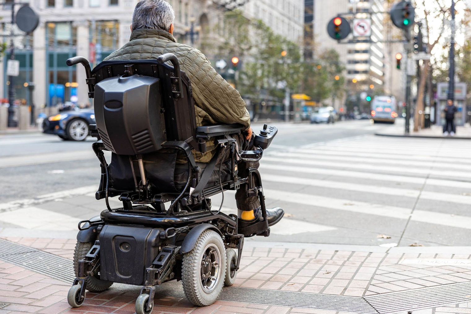 Person i elektrisk rullestol på vei ut i et gangfelt i et bymiljø.