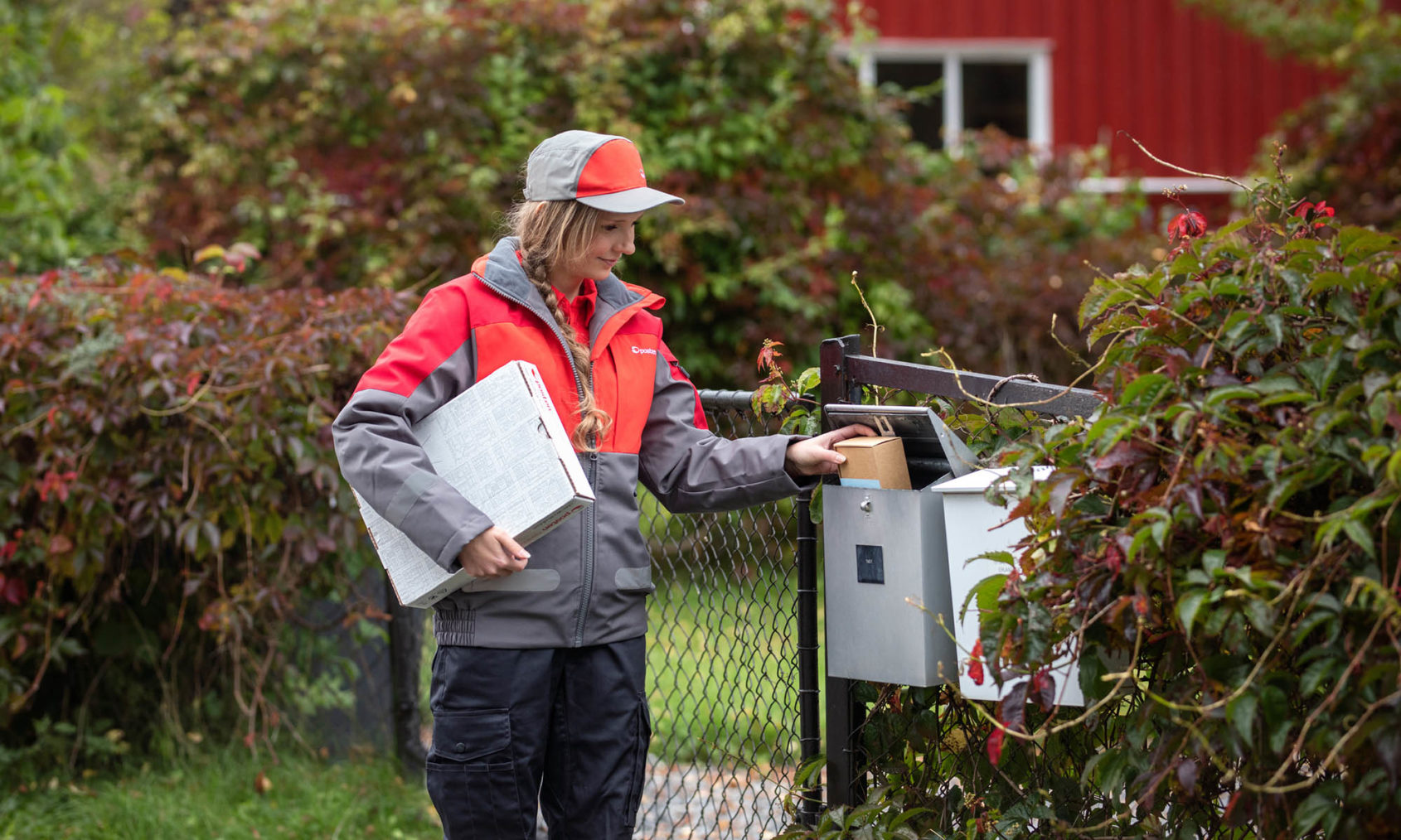 Postbud leverer post i en postkasse på et hagegjerde.