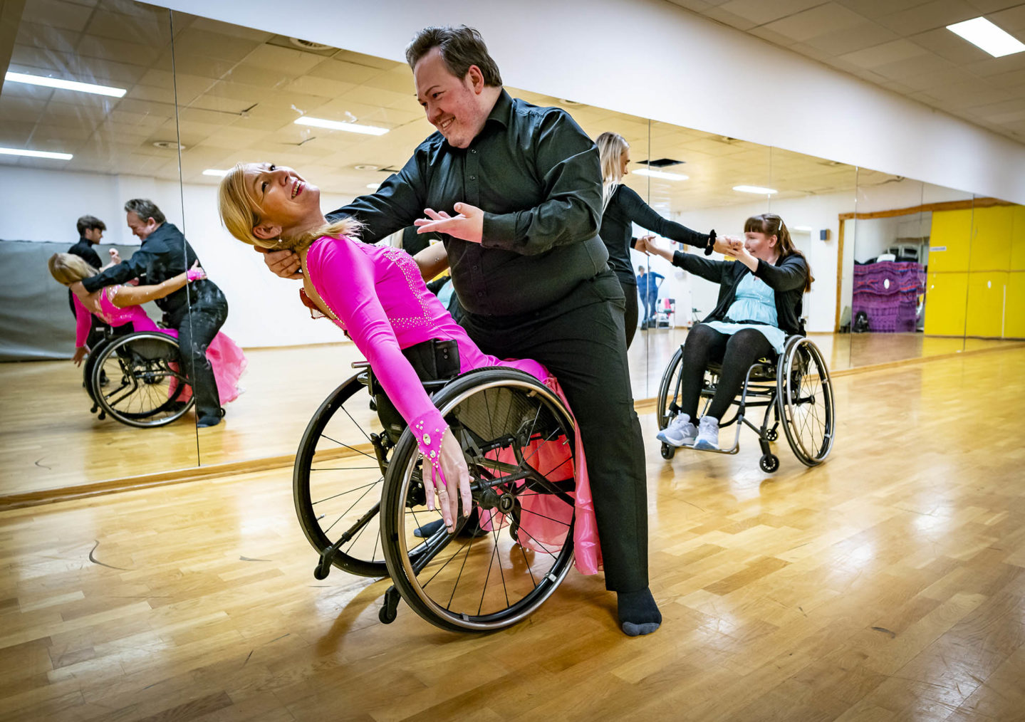 De to danser sammen. Hun i rullestol, han gående. Hun har på seg en rosa ballkjole med paljetter.