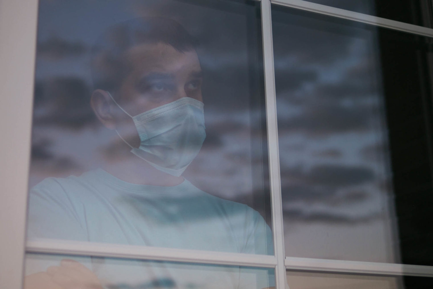 Mann med ansiktsmaske ser ut av et vindu.