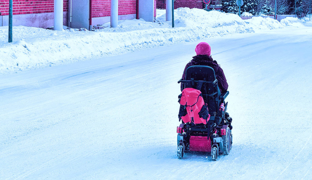 person i elektrisk rullestol på snødekt gate.