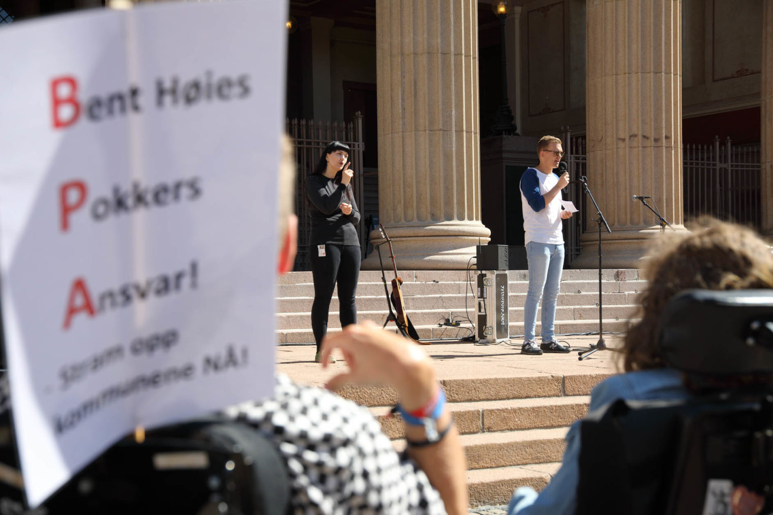 Bilde fra appell på Universitetsplassen i Oslo. I forgrunnen: rullestolbruker med plakaten "Bent Høies Pokkers Ansvar – Stram opp kommunenen NÅ!"