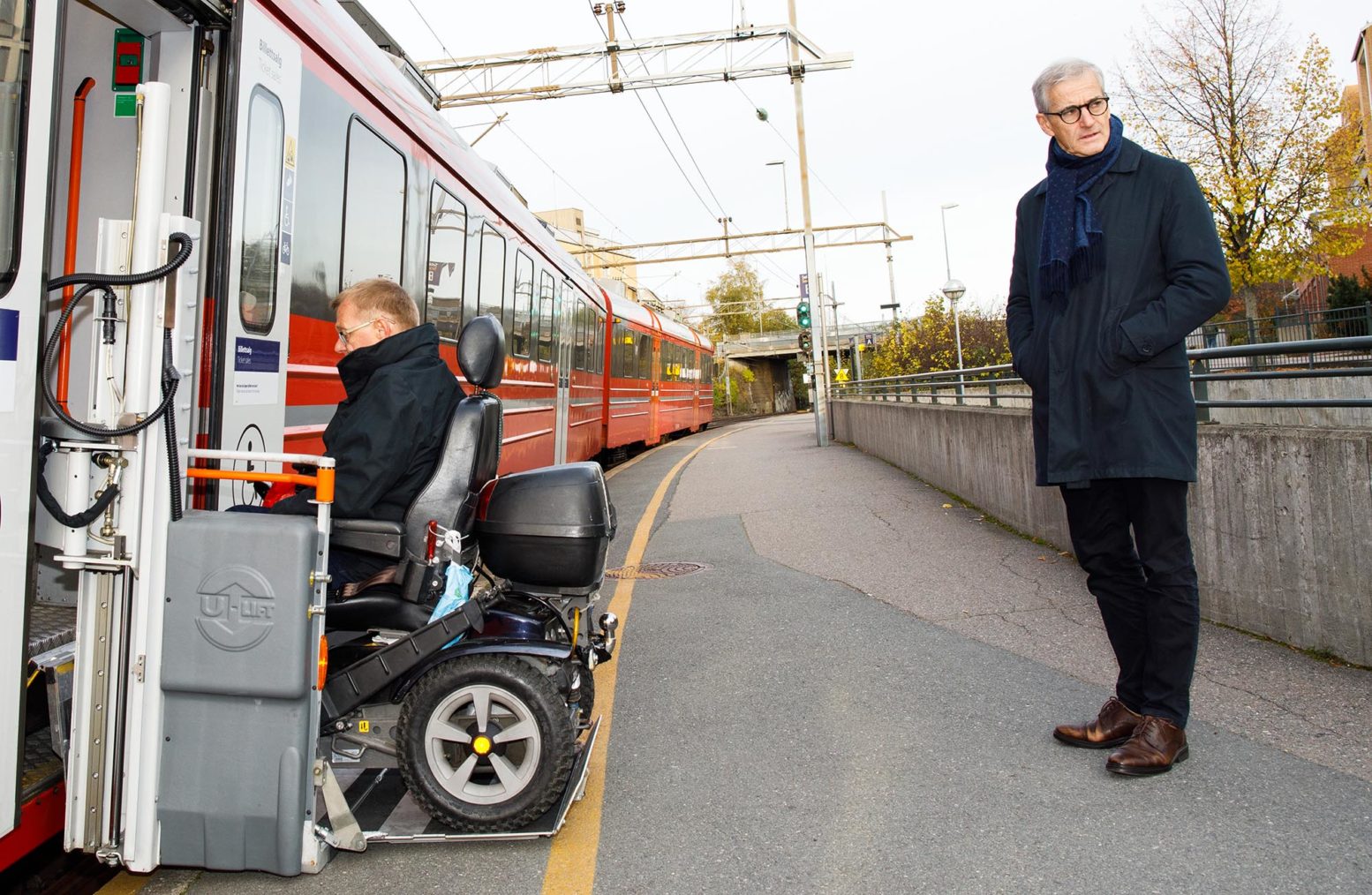 Støre på perrongen mens Haarstad kjører rullestolen inn på togets heis.