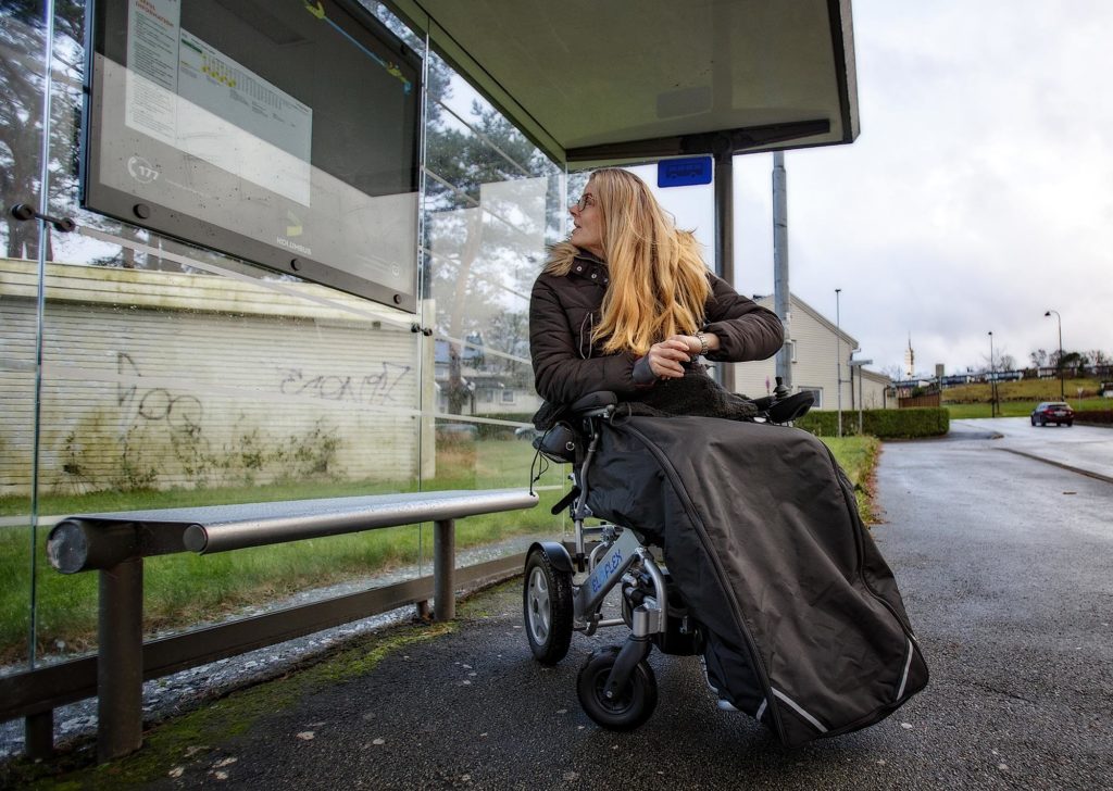 Gro Maren på bussholdeplass. Hun studerer rutetabellen på veggen i busskuret.