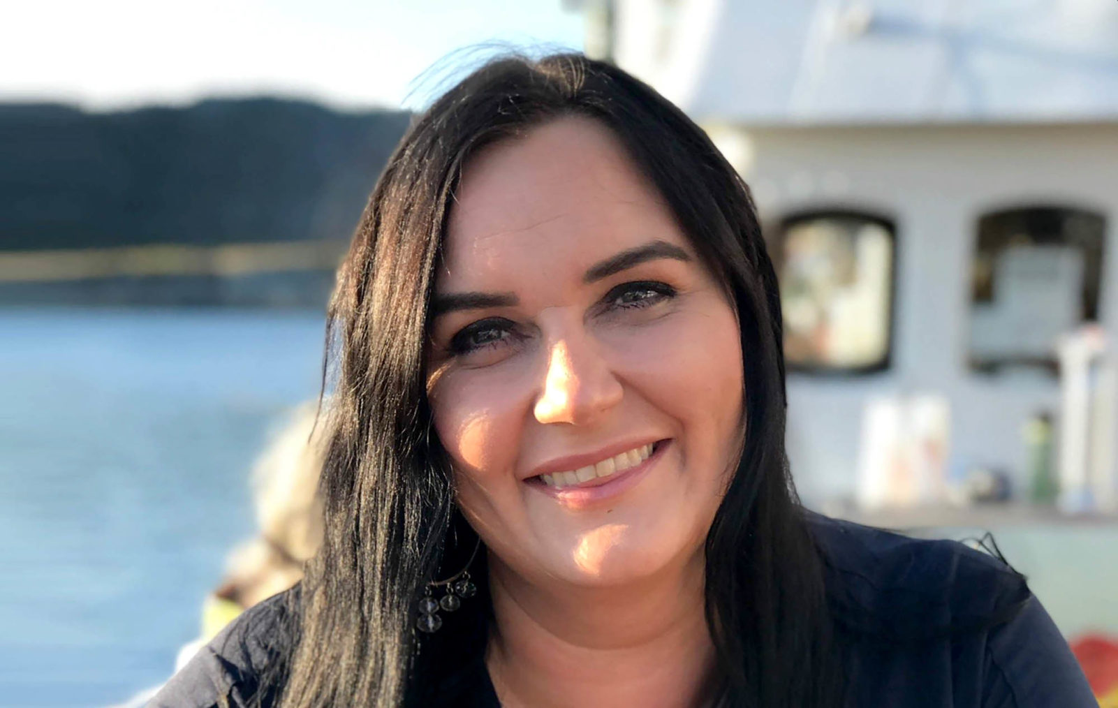 Portrett av Monica Tangen. I bakgrunnen skimtes sjøen og en fiskeskøyte.