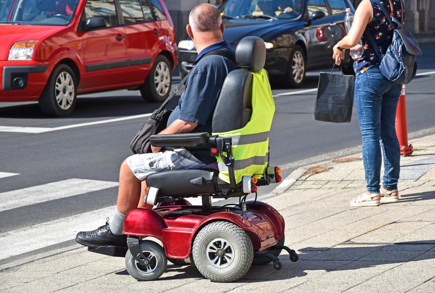 bilde av mann i elektrisk rullestol som skal krysse en gate.