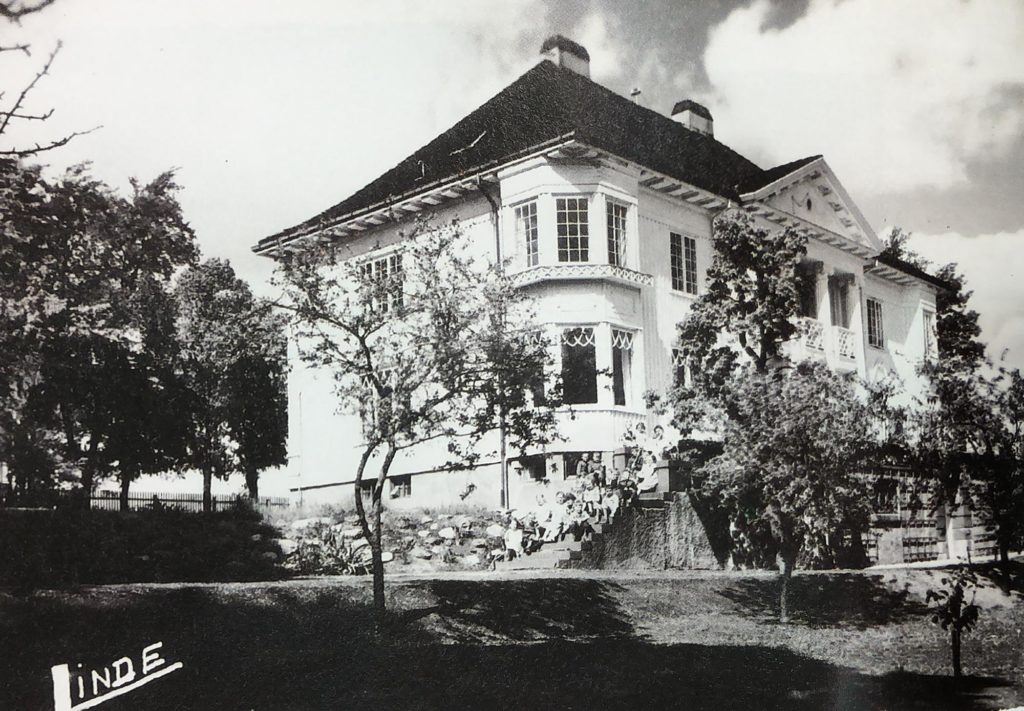 Bilde av bygningen, en hvit, herskapelig villa med veranda. Huset ligger i en stor hage.