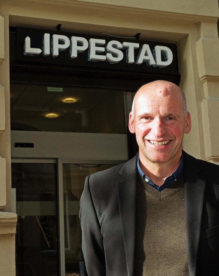 Geir Lippetad foran inngangsdøren til kontoret sitt. På veggen over døren er logoen «Lippestad».