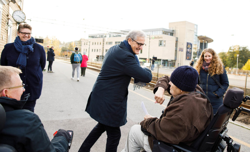 Jonas Gahr Støre hilser smilende på rullestolbrukere.