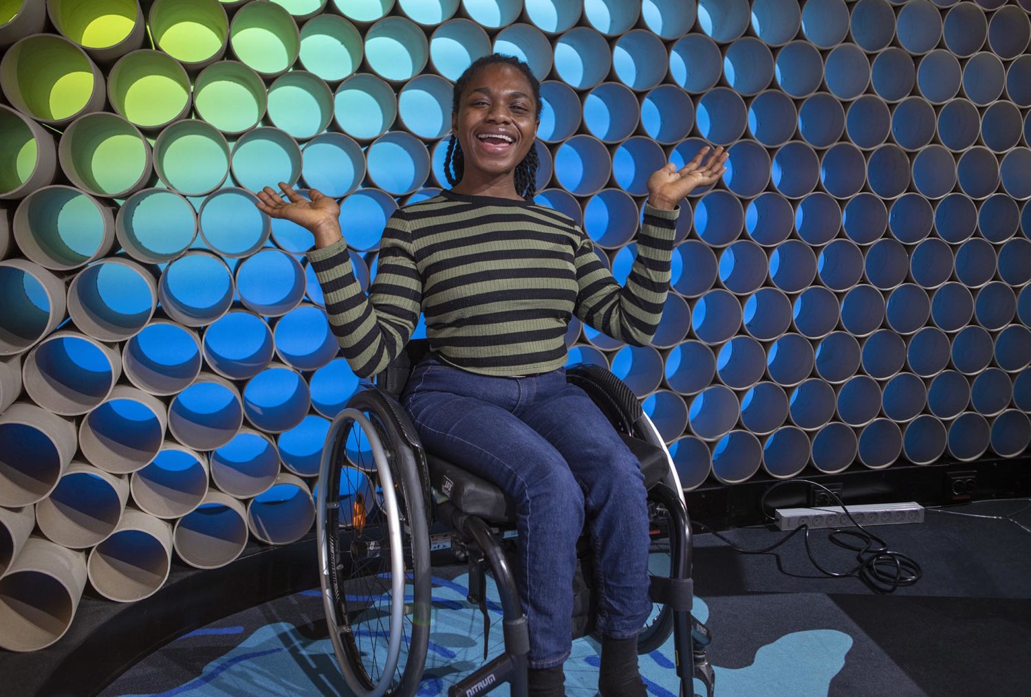 Smilende Sally i rullestol foran kullissene i et TV-studio.