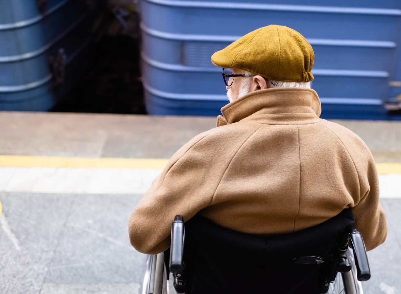 Eldre mann i rullestol på en jernbaneperrong ser på et passerende tog.