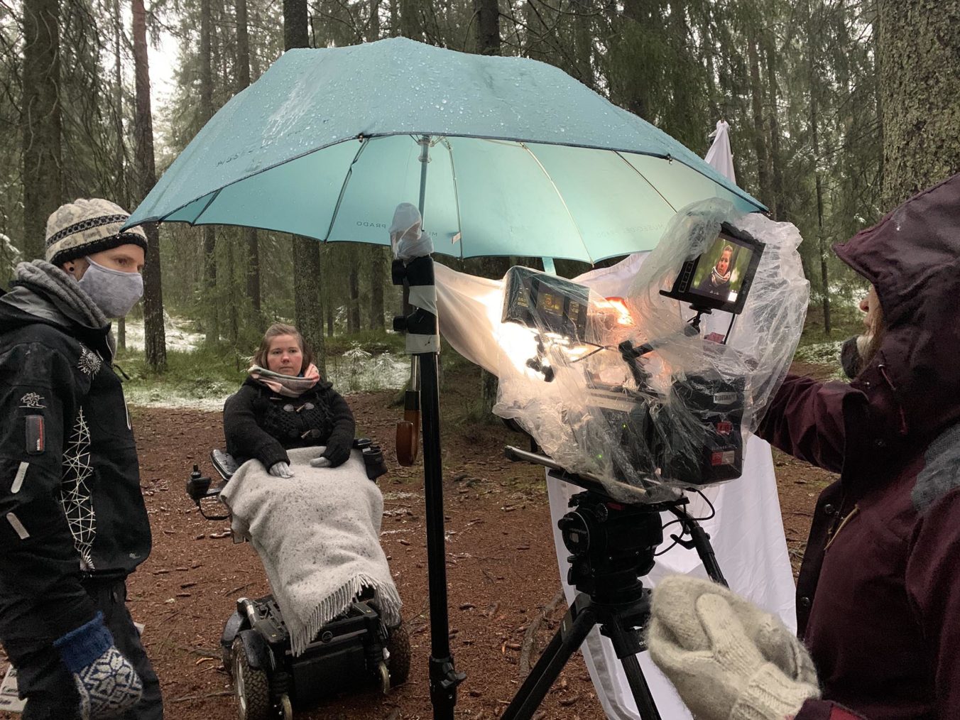 Bilde fra filmsett i skogen. Paraply over kameraet. Lena i rullestol.