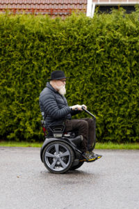 Oddgeir kjører stolen på en vei. Fotografert i profil.