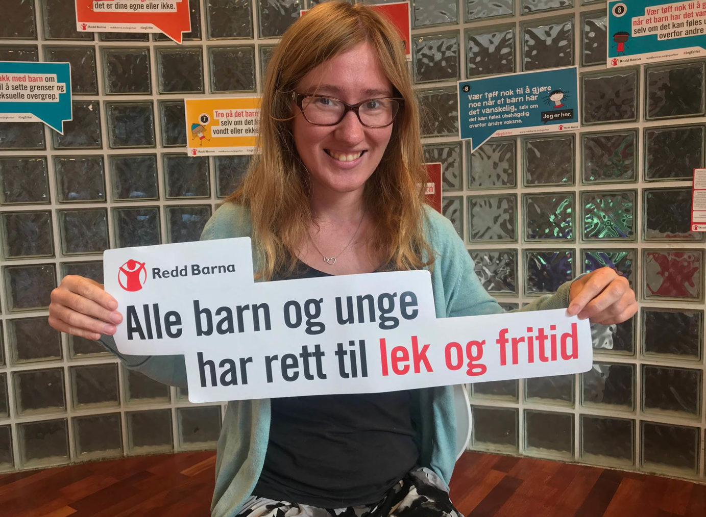 Martine Eliasson holder opp et skilt med Redd Barnas logo og teksten: Alle barn og unge har rett til lek og fritid.