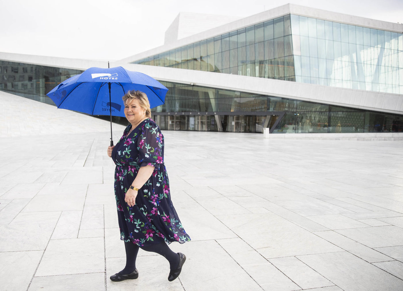 Erna Solberg med blå paraply med Høyre-logo på Operataket i Oslo.