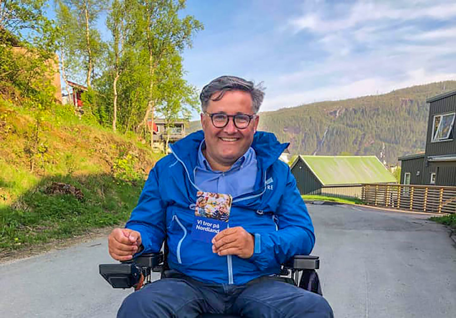 Gaute Ove Larsen i elektrisk rullestol. Han holder en valgkampbrosjyre og har på seg blå jakke med Høyre-logo.