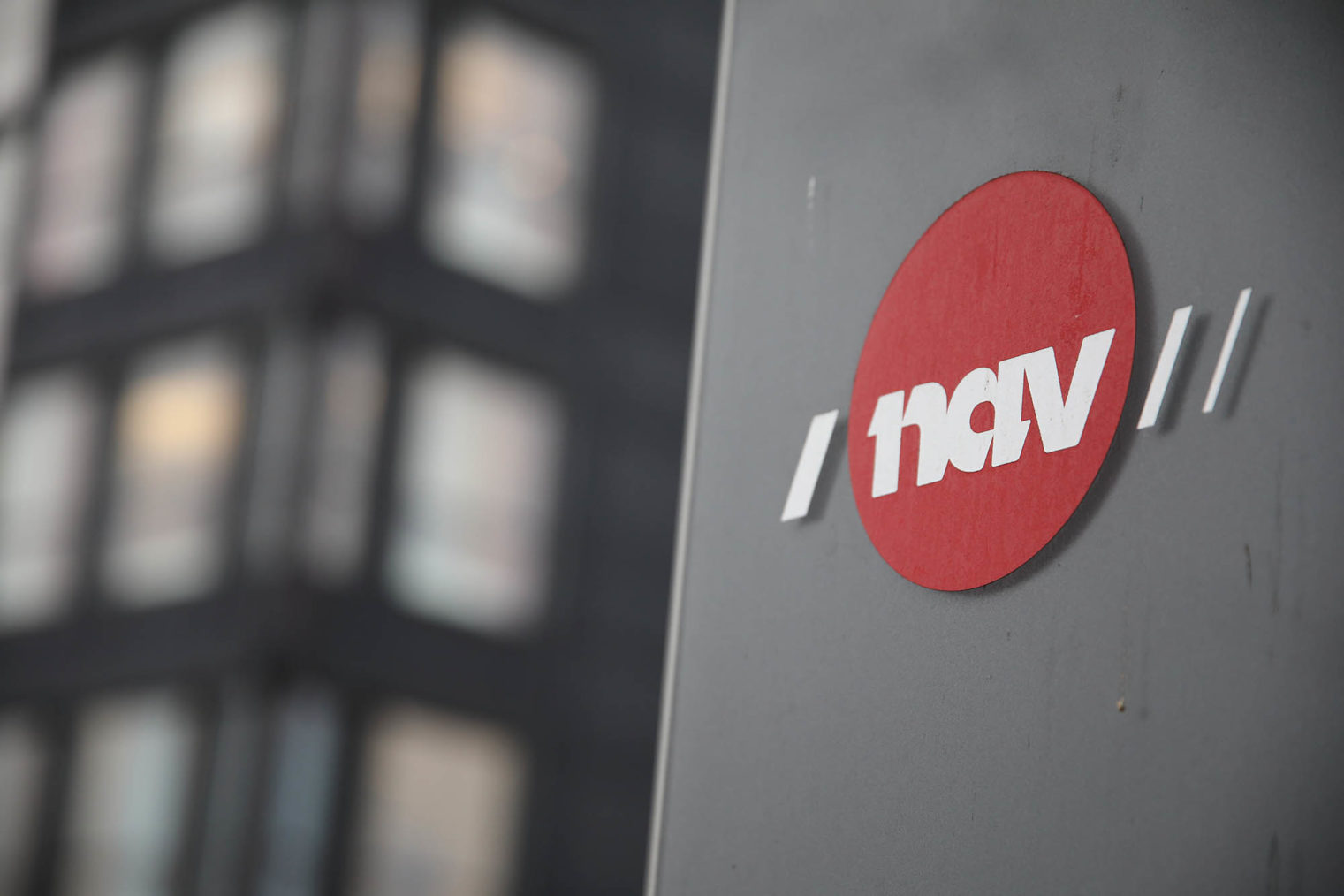 Detaljfoto av Nav-logo foran en stor kontorbygning.