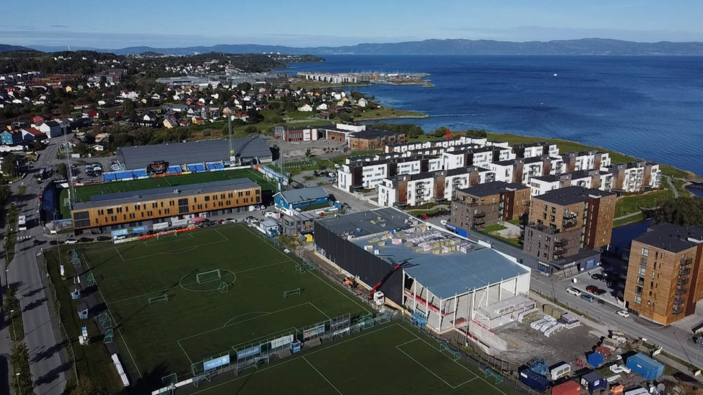 Dronebilde som viser den nye hallen og omgivelsene med flere nye boligblokker og Trondheimsfjorden i bakgrunnen.