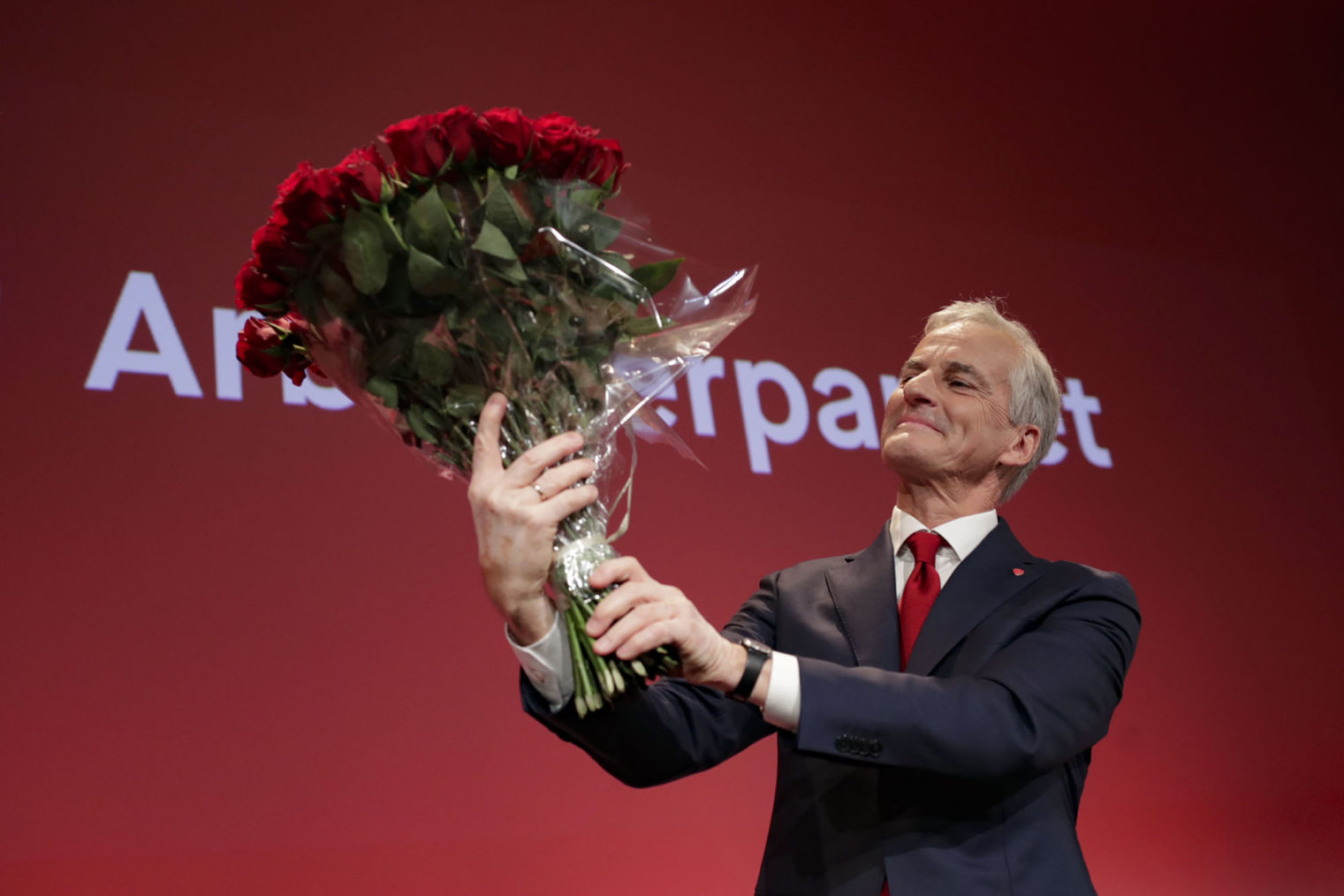Jonas Gahr Støre holder opp en bukett roser. I bakgrunnen Arbeiderpartiets logo.
