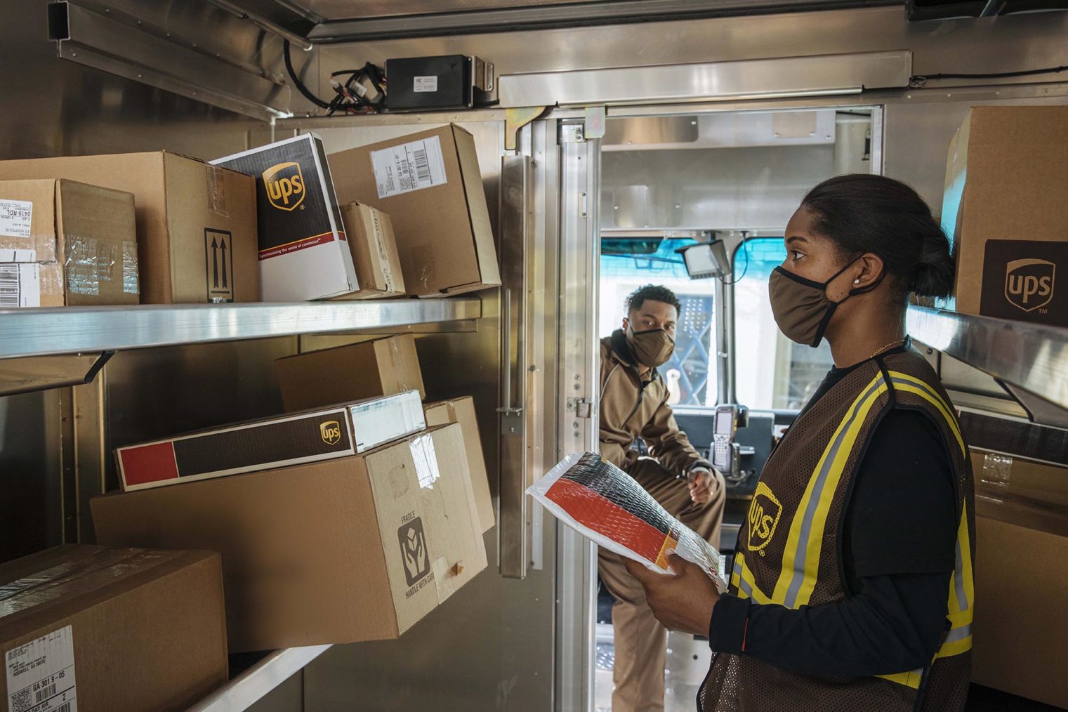 Bilde av to UPS-ansatte som sorterer pakker i en varebil.