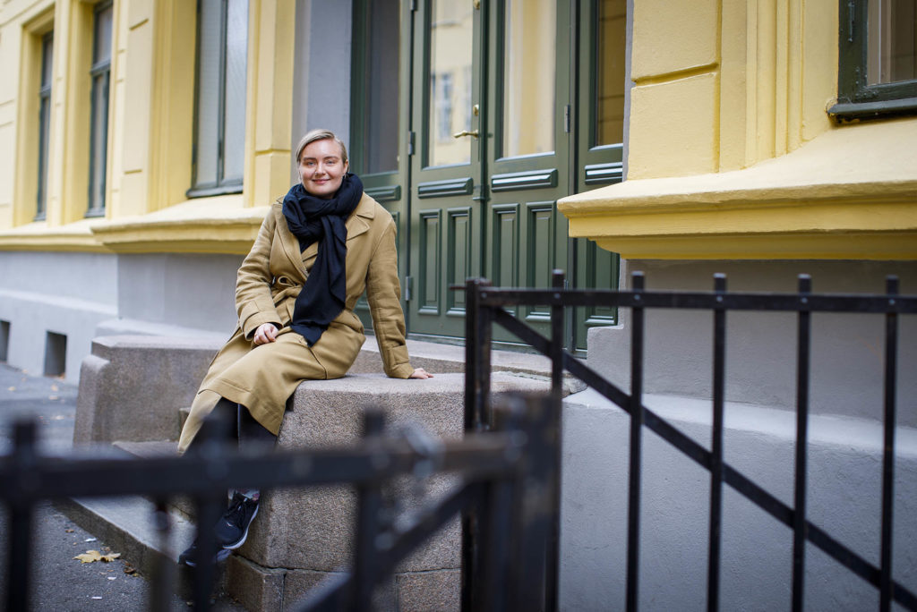 Maren Hagen Fuglesang sitter på en trapp inn til en skole. I forgrunnen en halvåpen jernport.