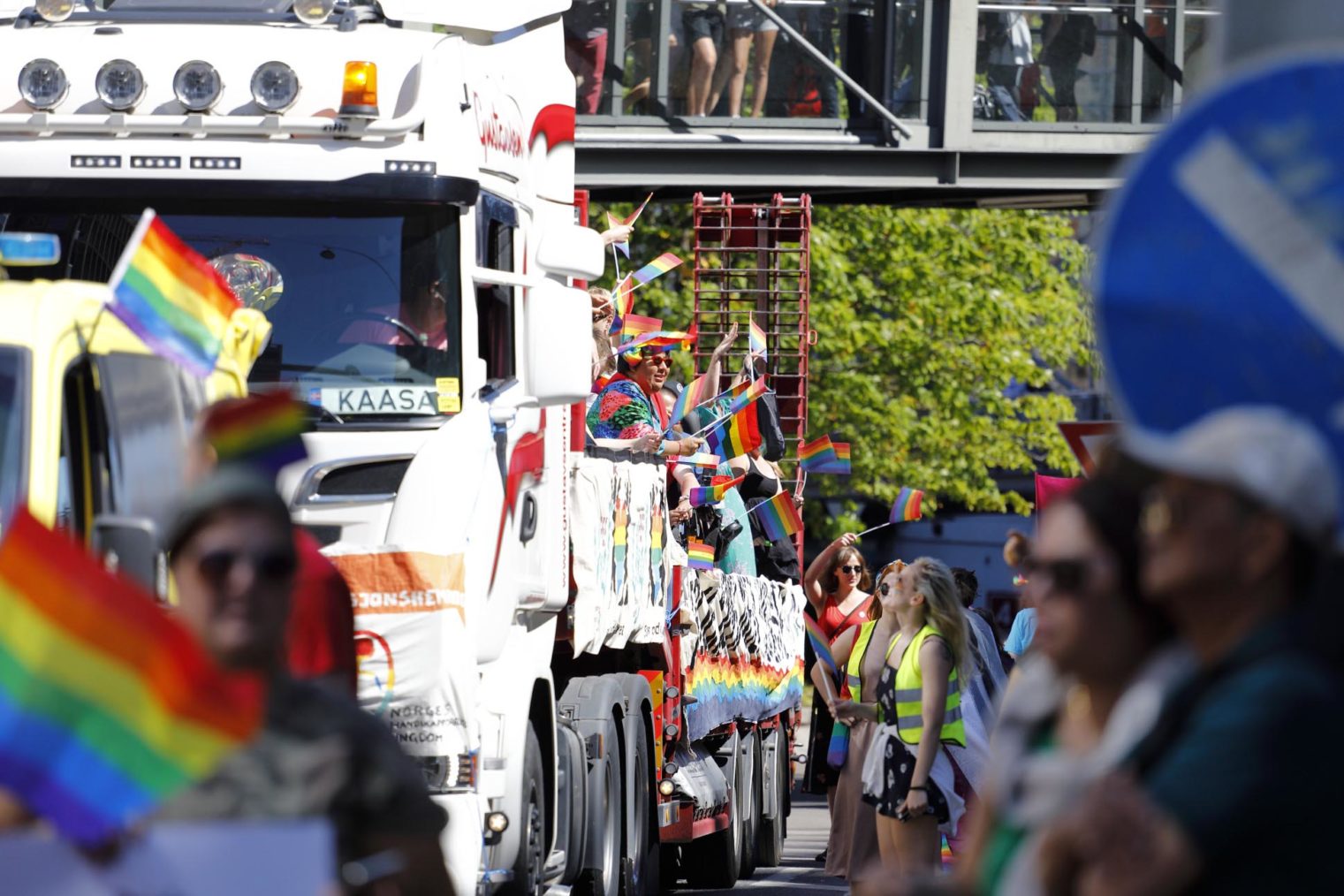 Bilde av lastebil gjennom folkehav. På planet sitter en masse mennesker og vinker med regnbueflagg.