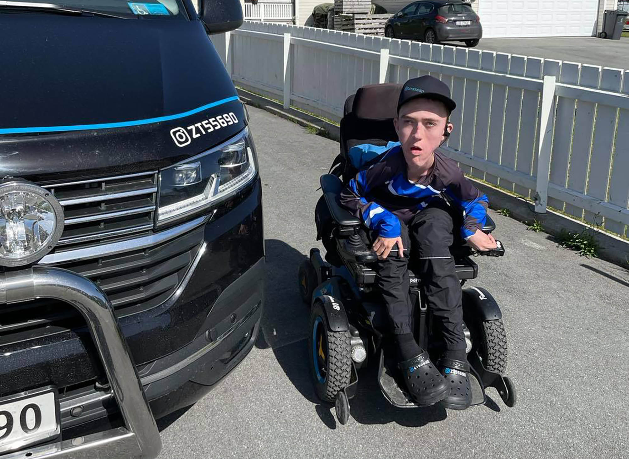 Joakim Øvergård i elektrisk rullestol ved siden av bilen sin.