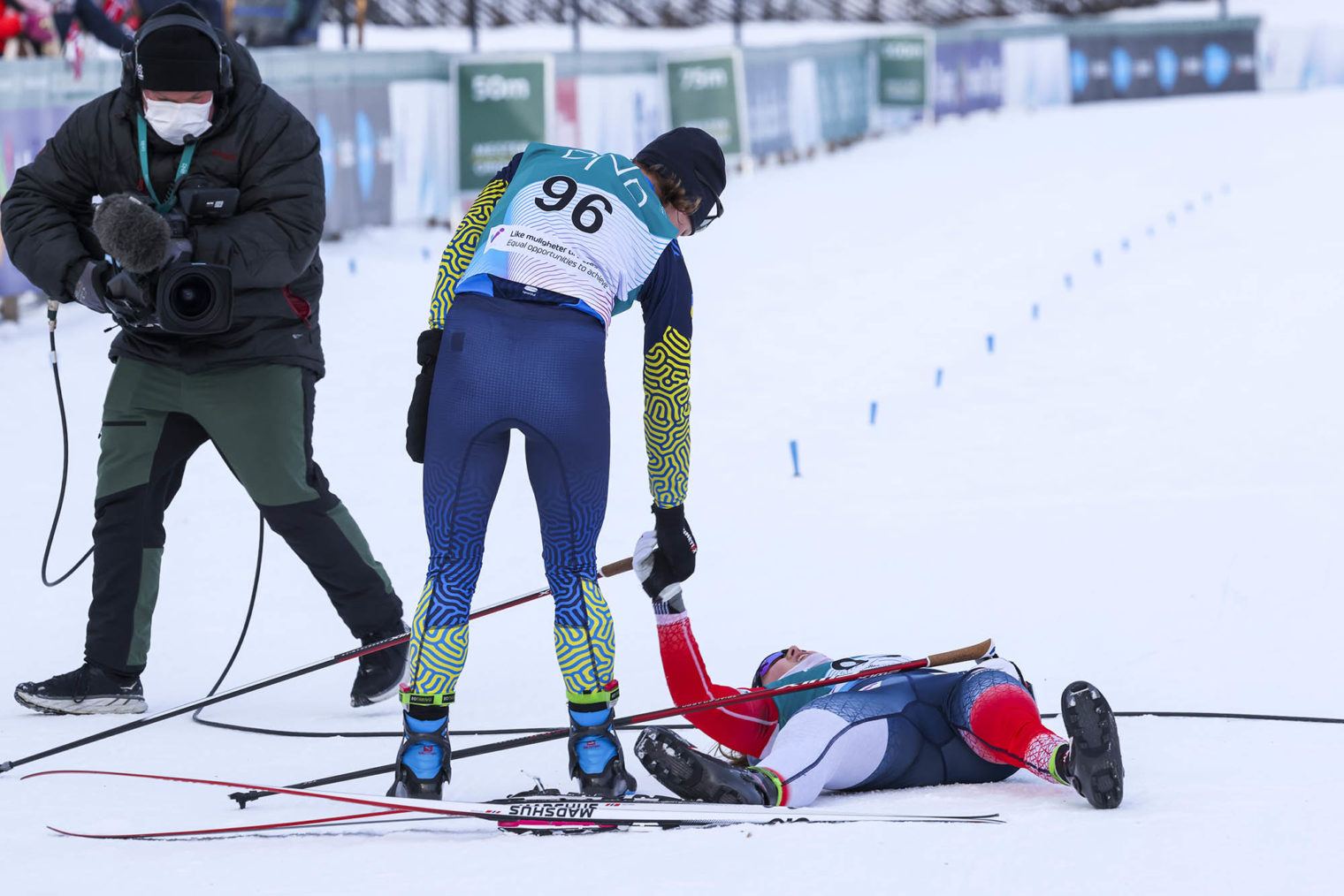 Vilde Nilsen ligger rett ut på snøen. Ludmila rekker henne hånden for å hjelpe henne opp.