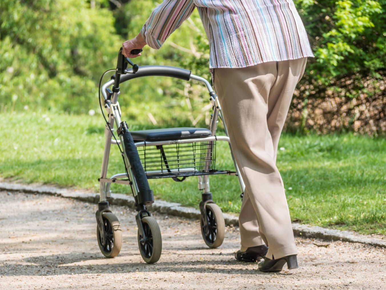 Detaljbilde av eldre kvinne som går tur i parken med rullator.