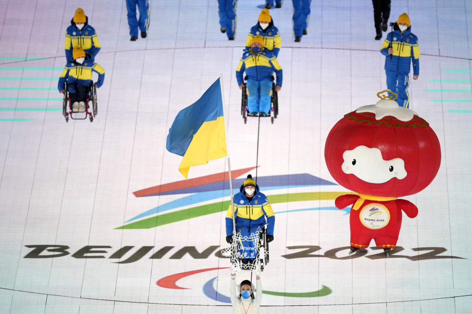 Troppen marsjerer inn på stadion med ukrainske flagg, ledsaget av en Paralympics-maskot.