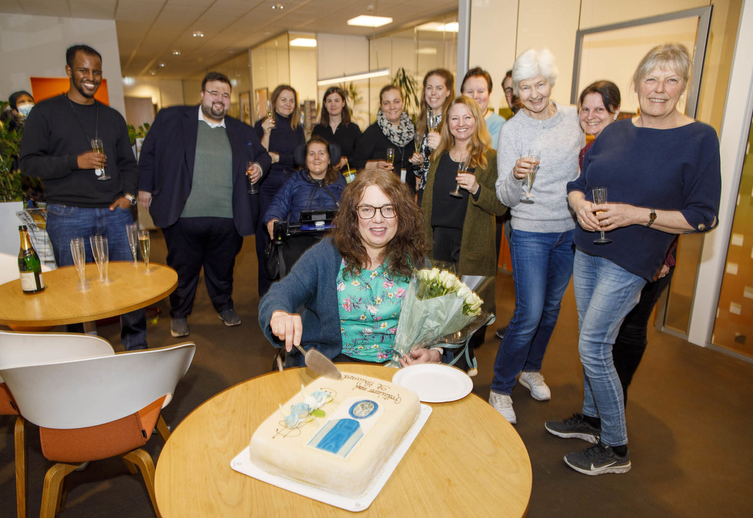 Magnhild Sørbotten skjærer et stykke kake mens ansatte står bak og smiler.