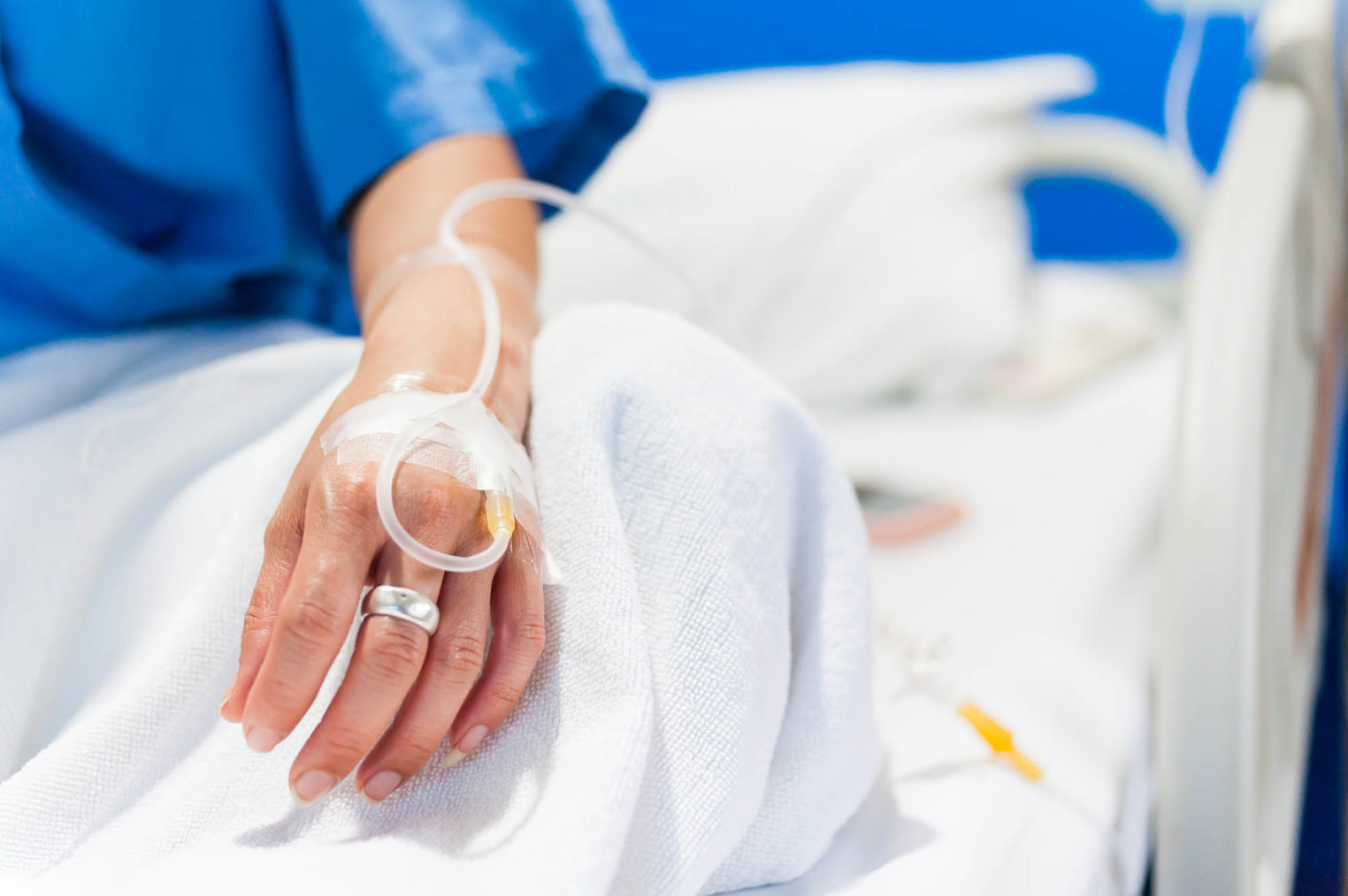 Nærbilde av hånd med veneflon i en sykehusseng.
