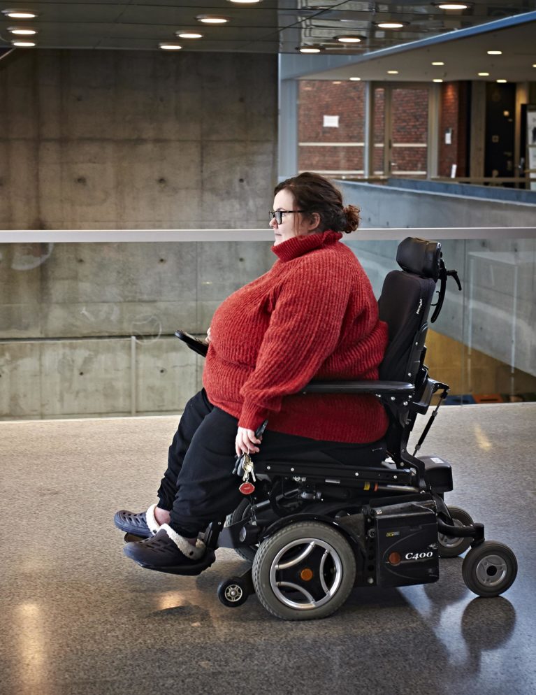 Sarah Naomi i elektrisk rullestol inne på høgskolen.