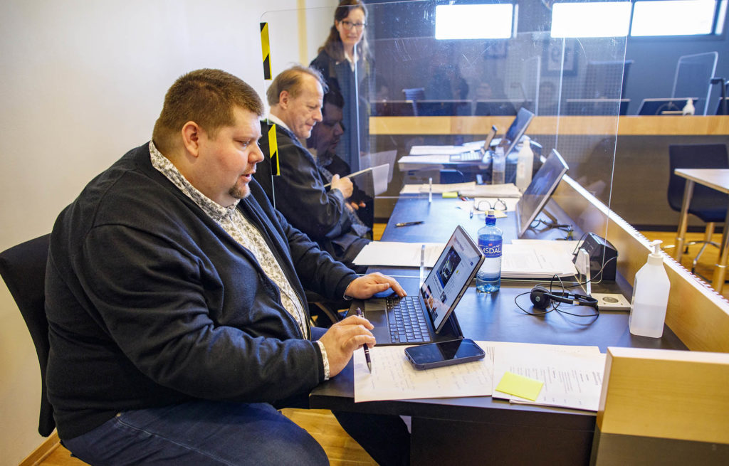 De tre ved et bord i rettssalen. Larsen skriver på en pc.