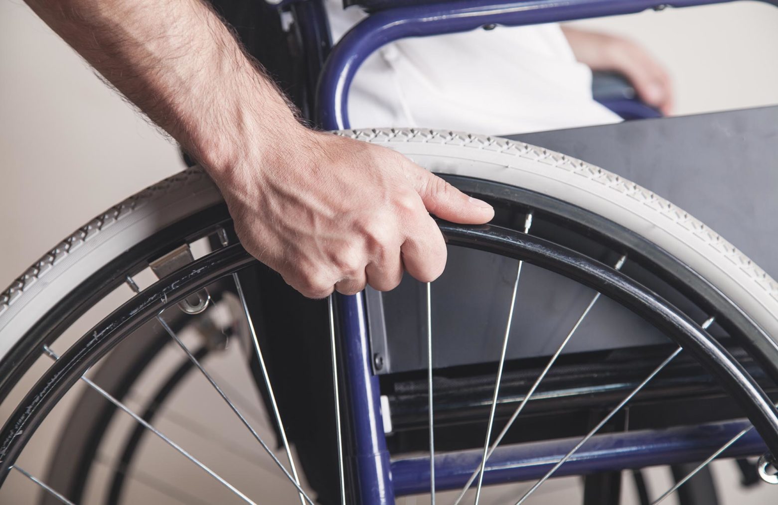 detaljfoto av person i rullestol med hånd på hjulet.